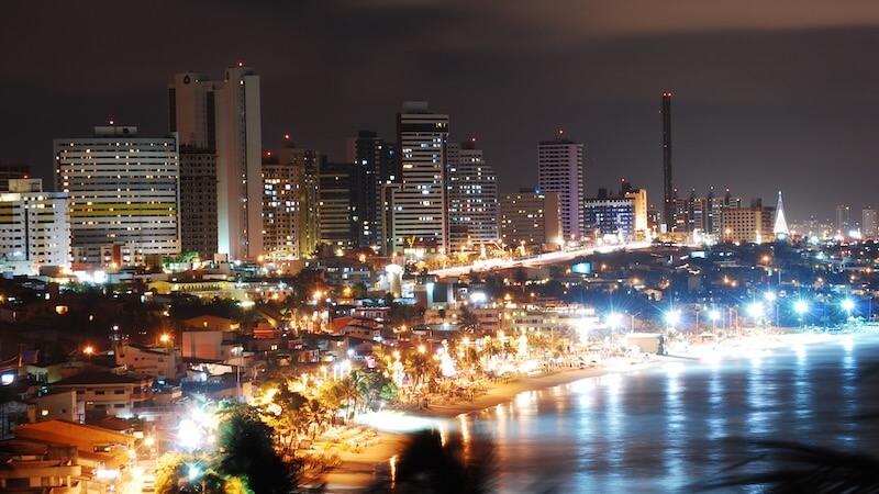 Imagem da cidade iluminada ao fundo e da praia à noite.