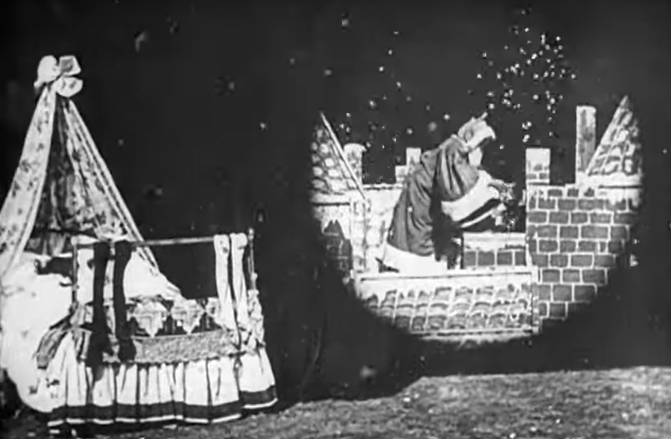 imagem preto e branco de uma parte do primeiro filme de natal registrado. De um lado mostra uma cama infantil, com duas crianças dormindo e meias penduradas à frente. Do outro lado, outra cena mostrando o Papai Noel entrando pela chaminé com uma árvore de natal enfeitada.
